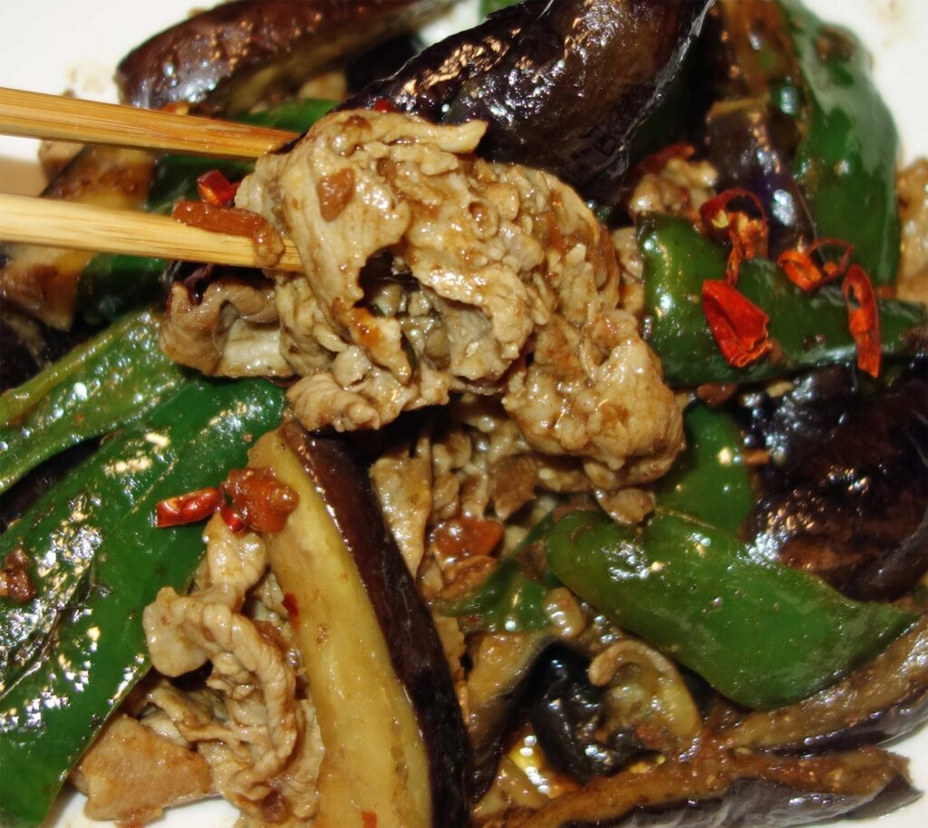 箸でつまんだ豚肉とナスとピーマンの炒め物