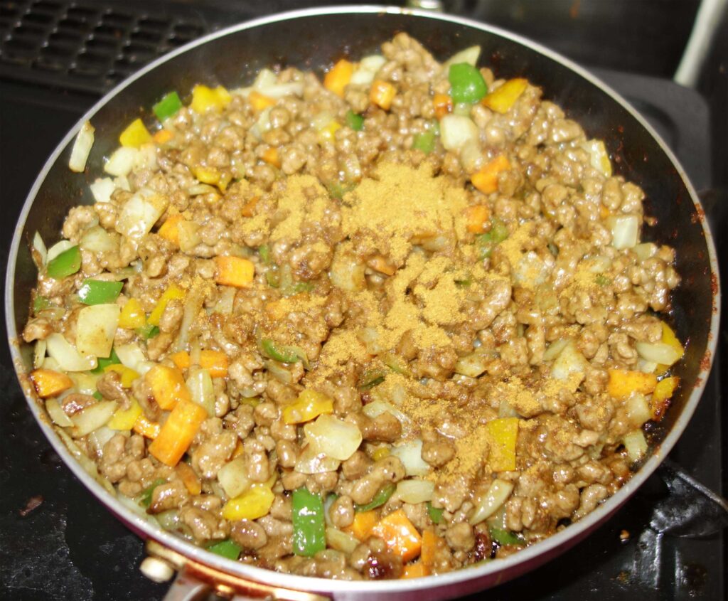 ひき肉と野菜の炒め物にカレー粉をかけている様子