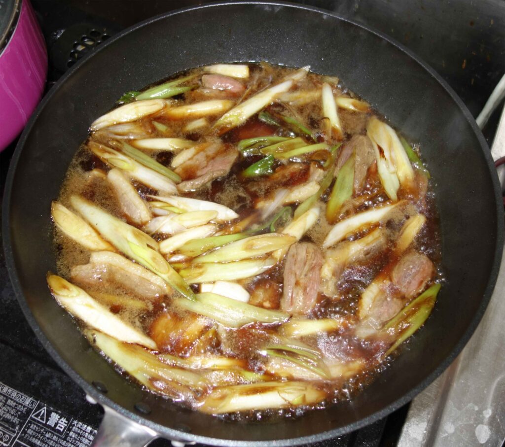 豚肉とネギを炒めているフライパン