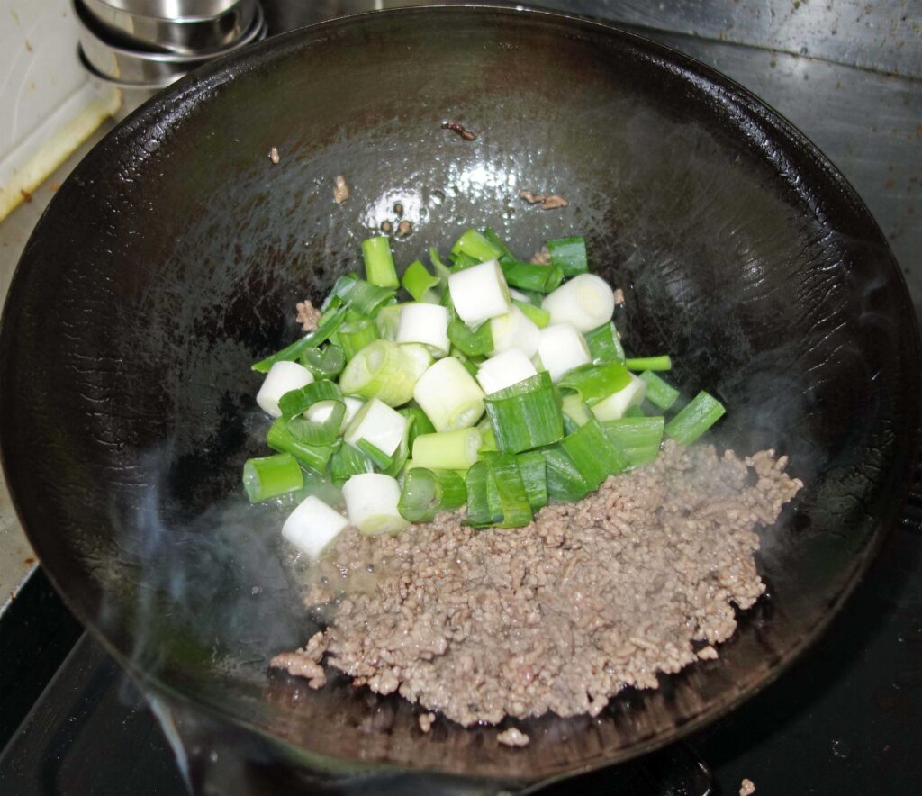 中華鍋で豚ひき肉とネギを炒める様子