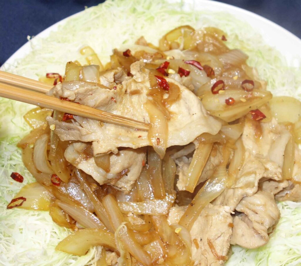 豚肉と玉ねぎ炒め物を箸で持ち上げている写真