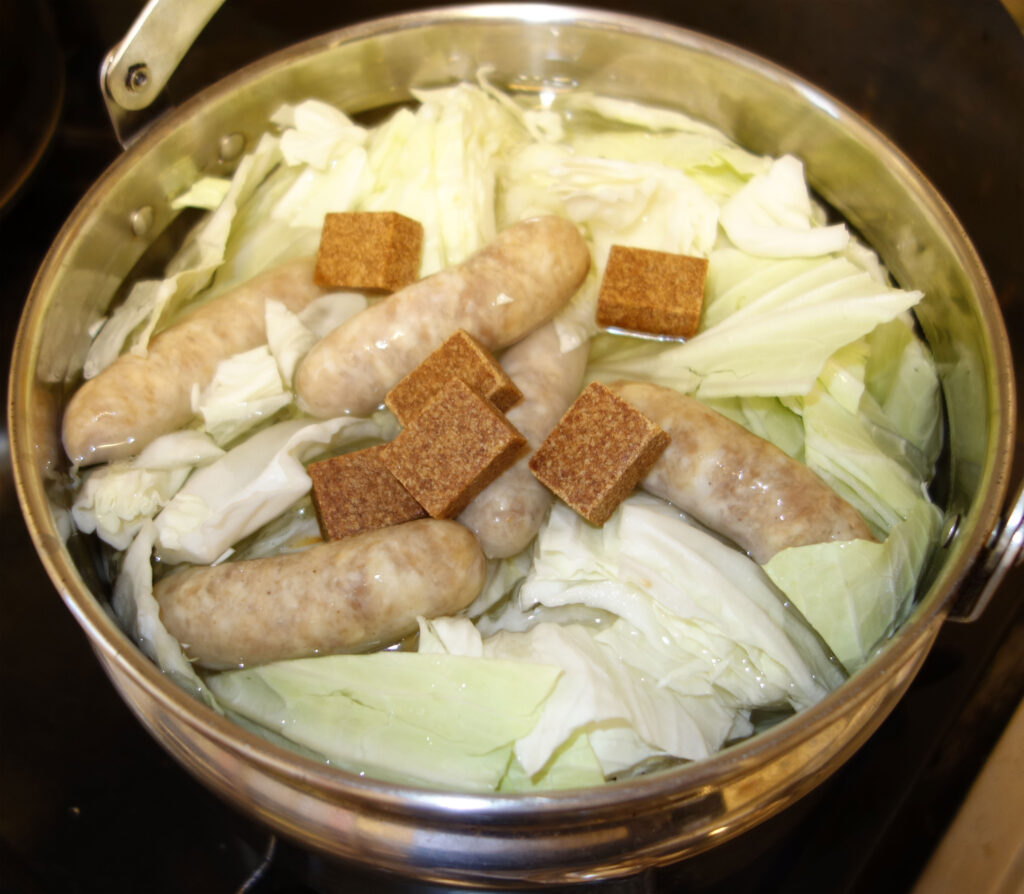 鍋に入ったソーセージとキャベツとスープの素