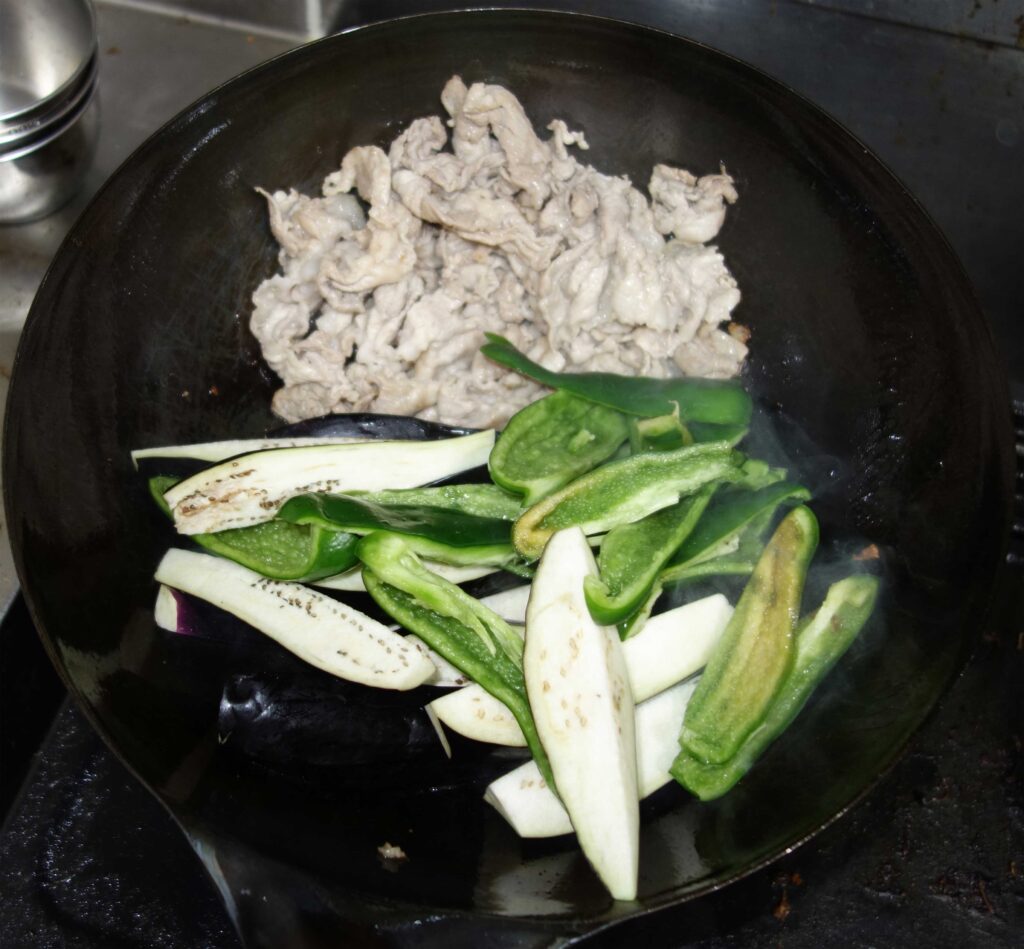 中華鍋で豚肉とナスとピーマンを炒めている様子
