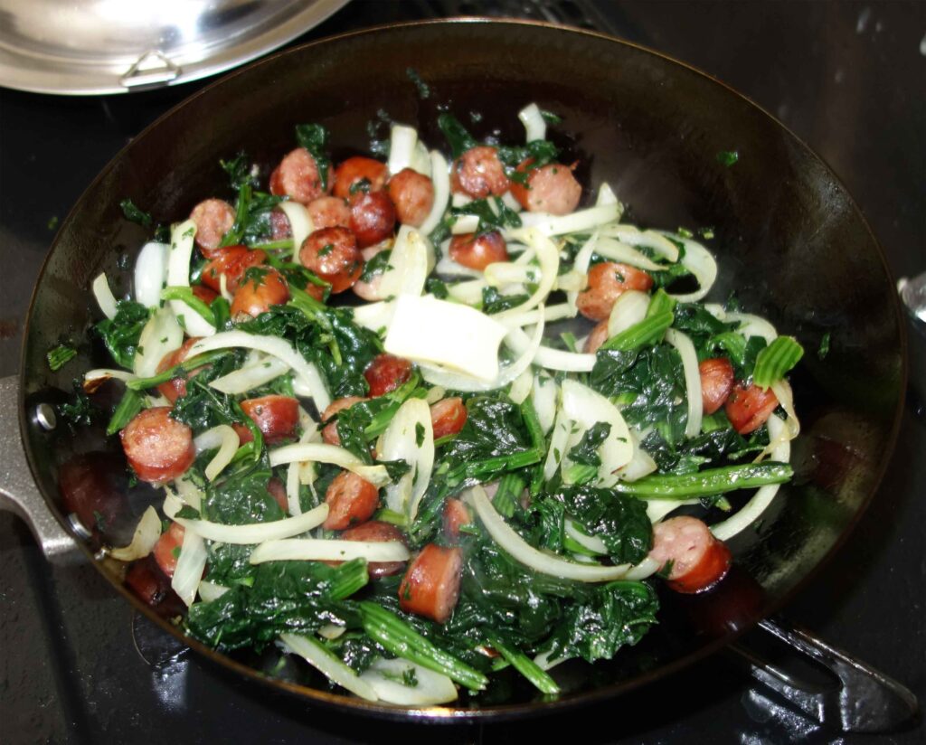 フライパンで炒めたソーセージとほうれん草と玉ねぎ