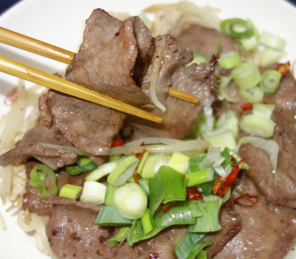 箸でつまんだ牛タン焼きとネギ