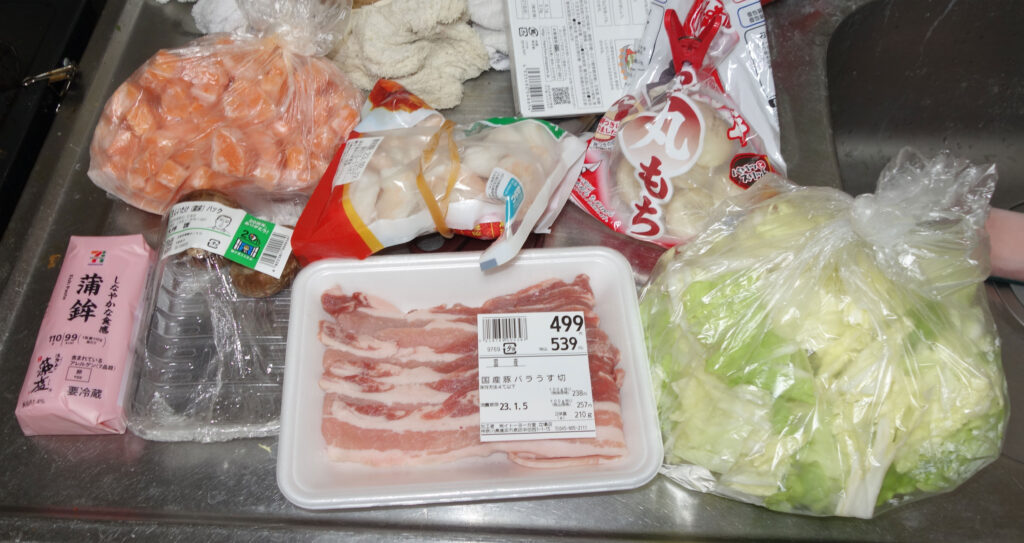 シンクに置かれた鮭切り身、豚バラ肉、キャベツなど食材