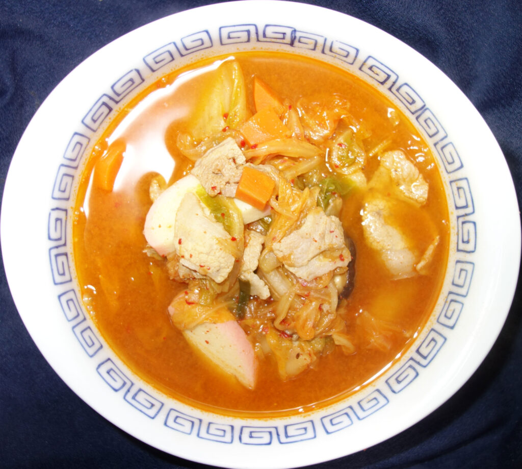 白地に青い模様の入ったどんぶりに盛られた豚肉と野菜入りのキムチ鍋