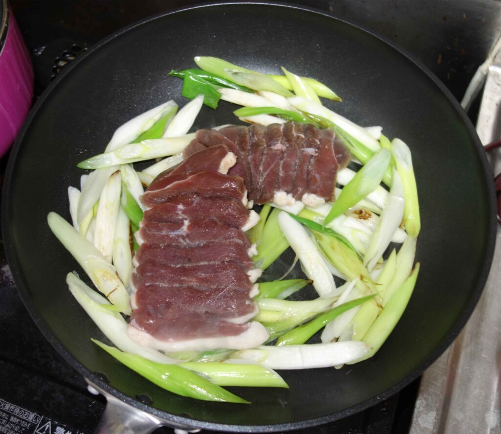 フライパンで焼かれた鴨肉とネギ