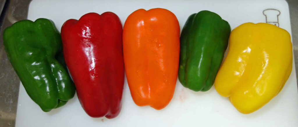 緑色、赤色、オレンジ色、緑色、黄色のパプリカがまな板に並んでいる写真
