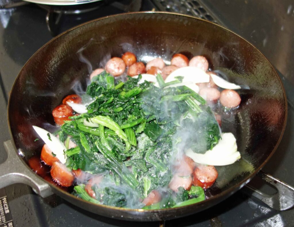 フライパンで炒められたソーセージ、ほうれん草、玉ねぎ