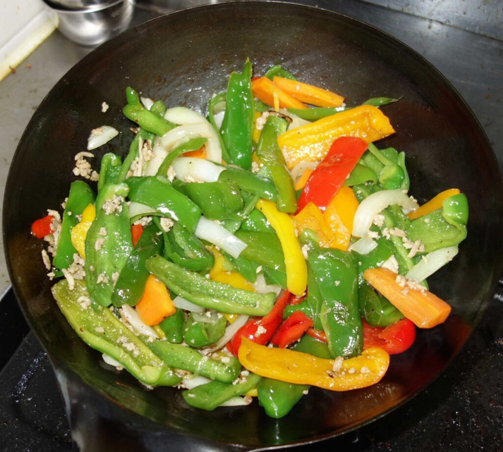 中華鍋で炒めたピーマンや玉ねぎなどの野菜炒め