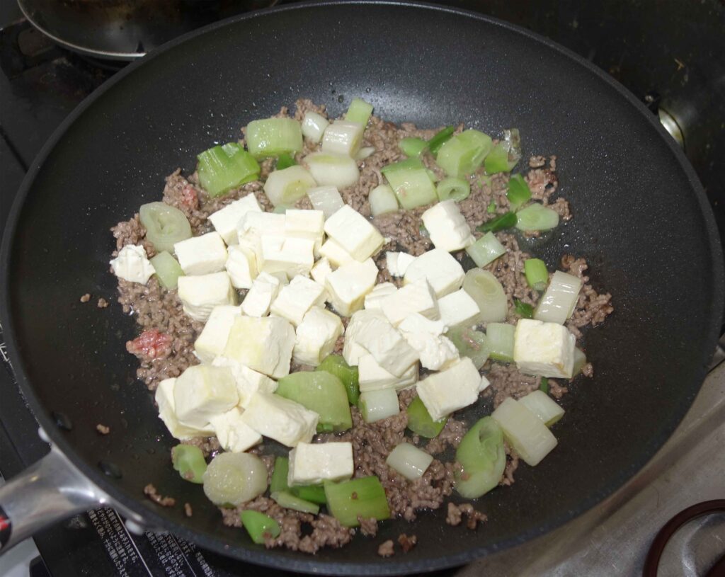 フライパンで豆腐とひき肉とネギを炒めている様子