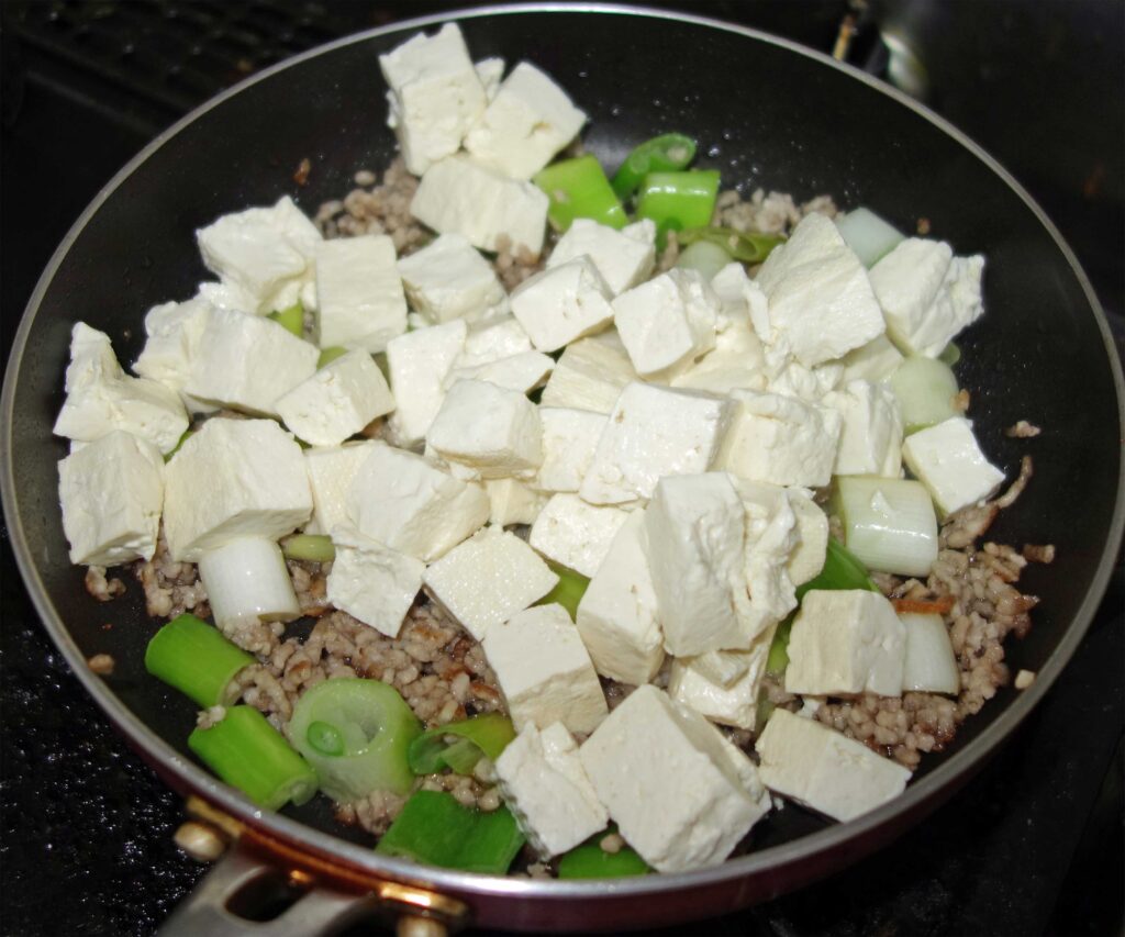 フライパンで豆腐とネギとひき肉を炒めている様子