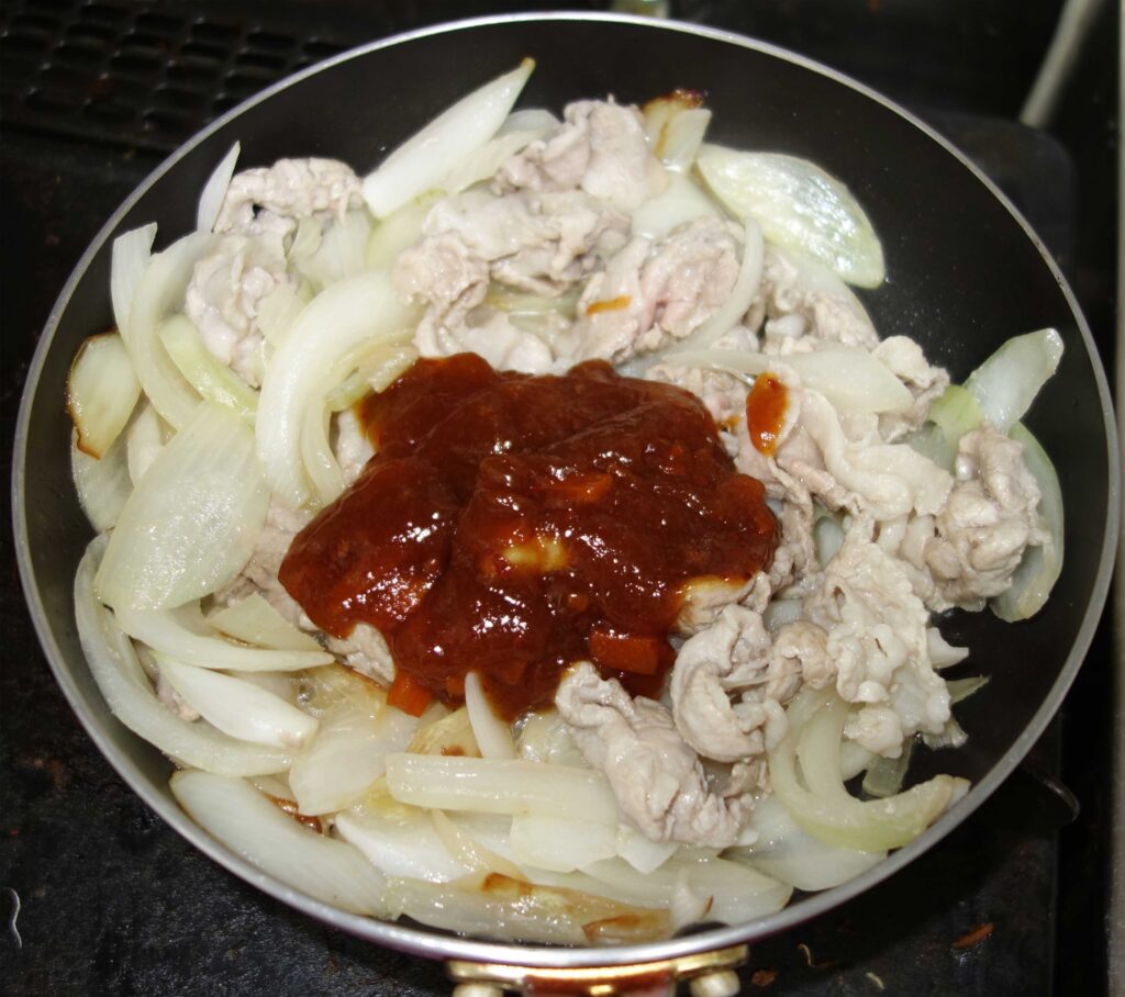 フライパンで豚肉と玉ねぎを炒め、ソースをかけた料理