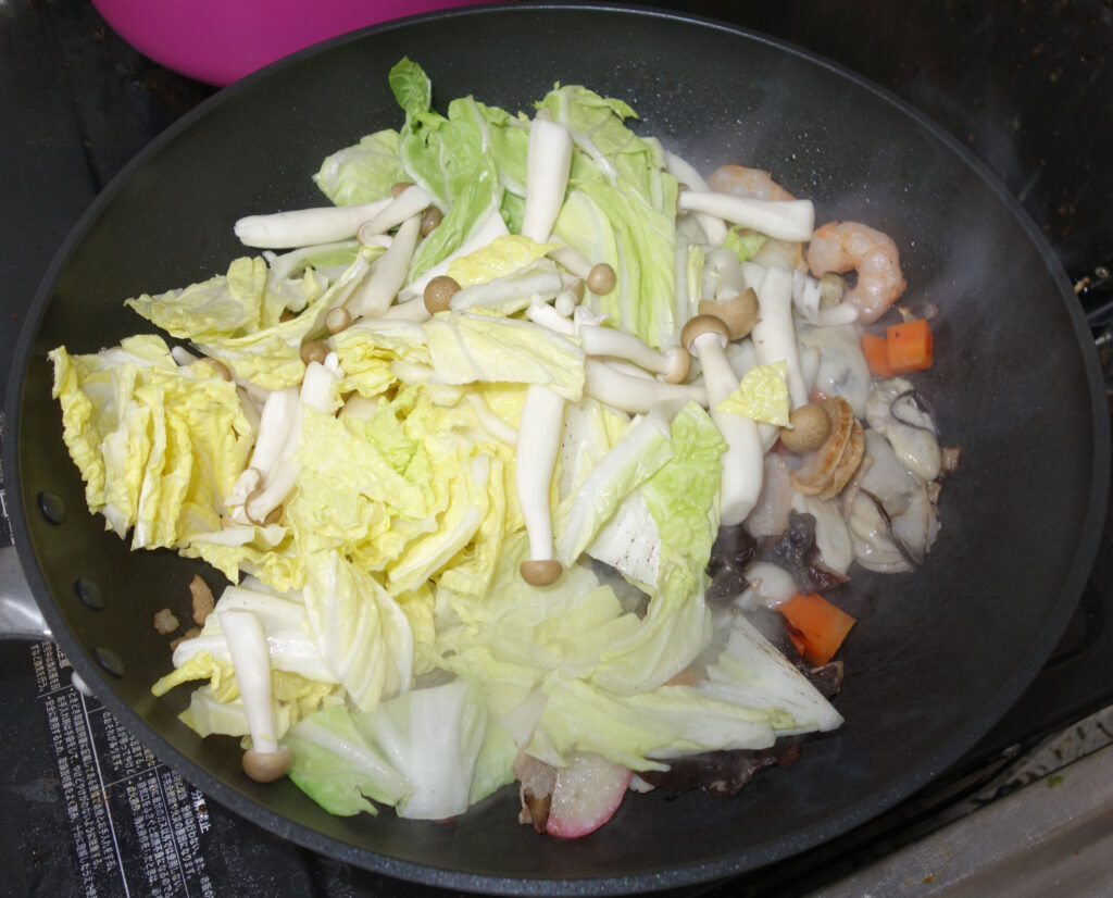 鍋で調理中の白菜やきのこ、エビ、カキ