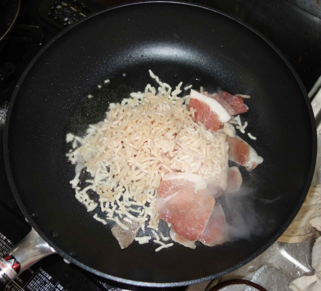 フライパンで豚肉と米状のパスタを炒める様子