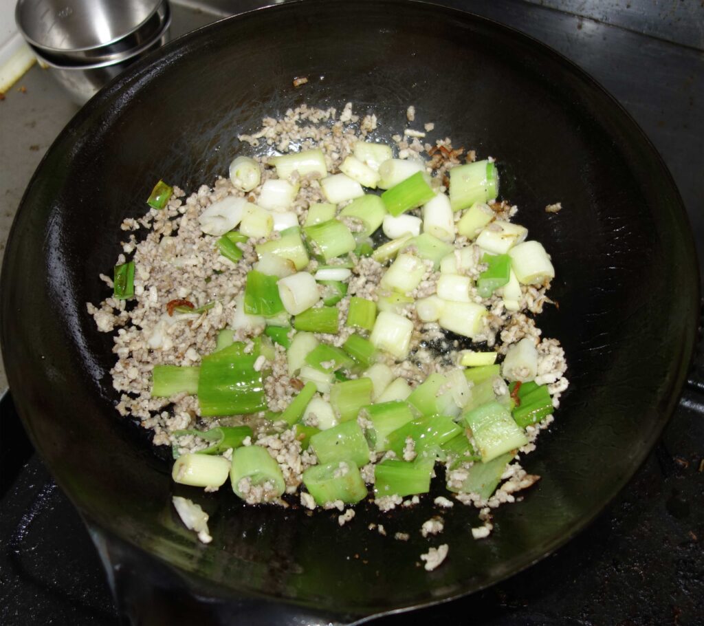 中華鍋で豚ひき肉とネギを炒めている様子