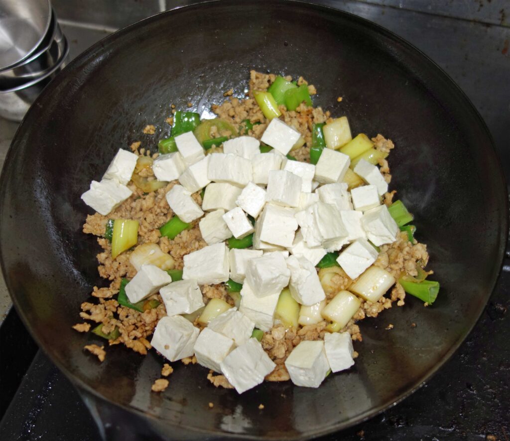 豆腐とひき肉とネギを炒めて豆腐を入れている様子