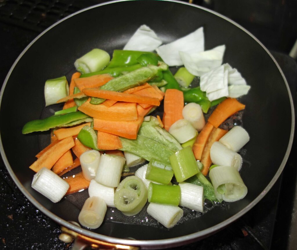 フライパンで炒めたニンジン、ピーマン、ネギ、キャベツ