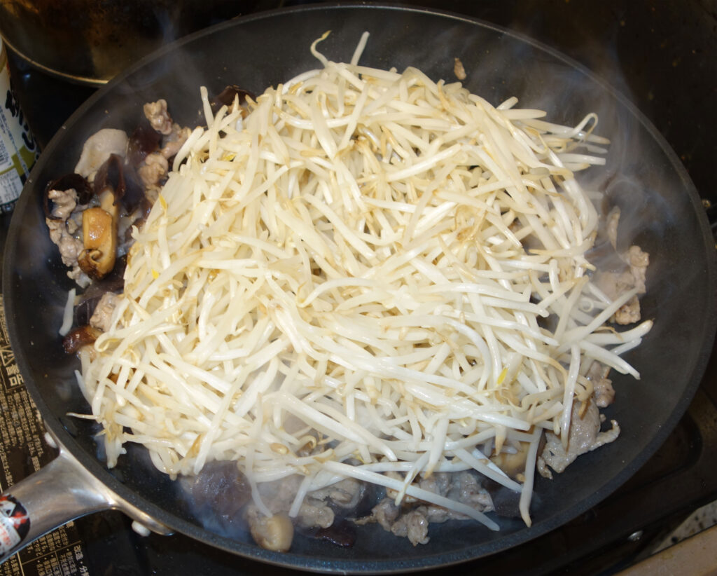 フライパンで豚肉ときくらげともやしを炒めている様子