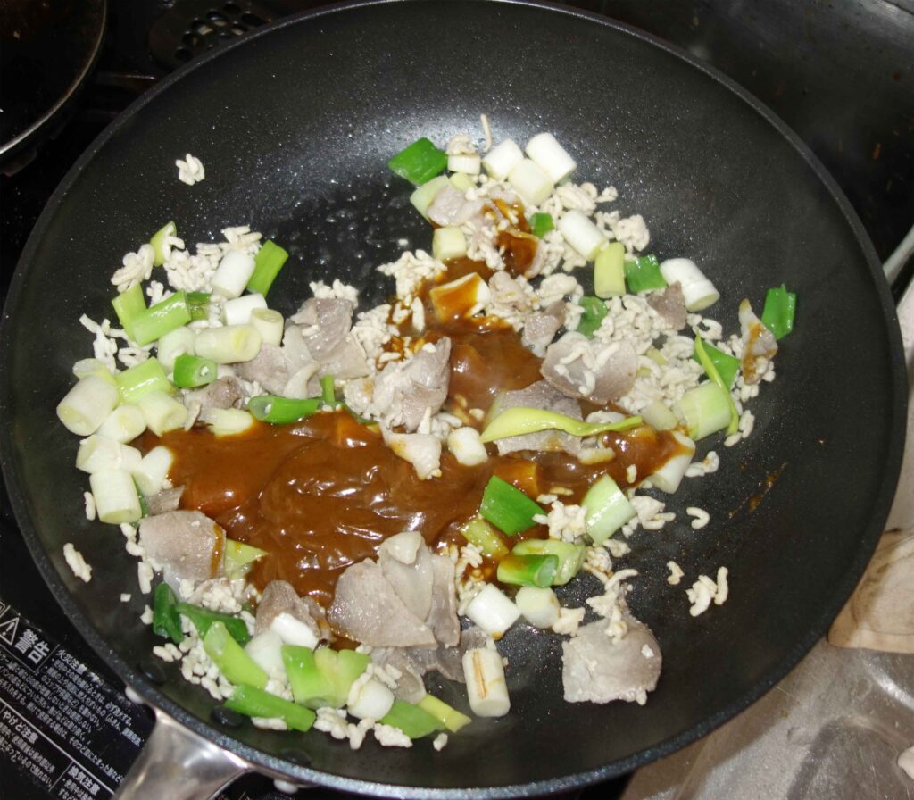 豚肉とネギとご飯を炒めているフライパン