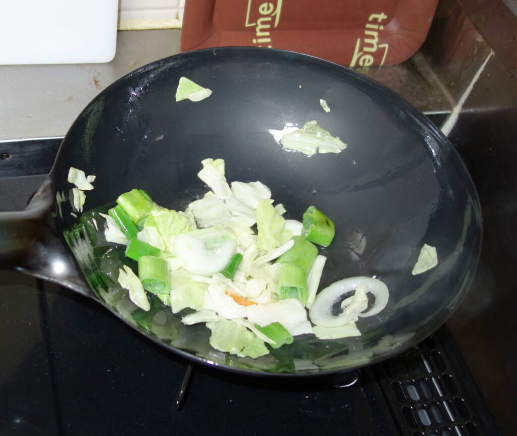 中華鍋でキャベツとネギを炒めている様子
