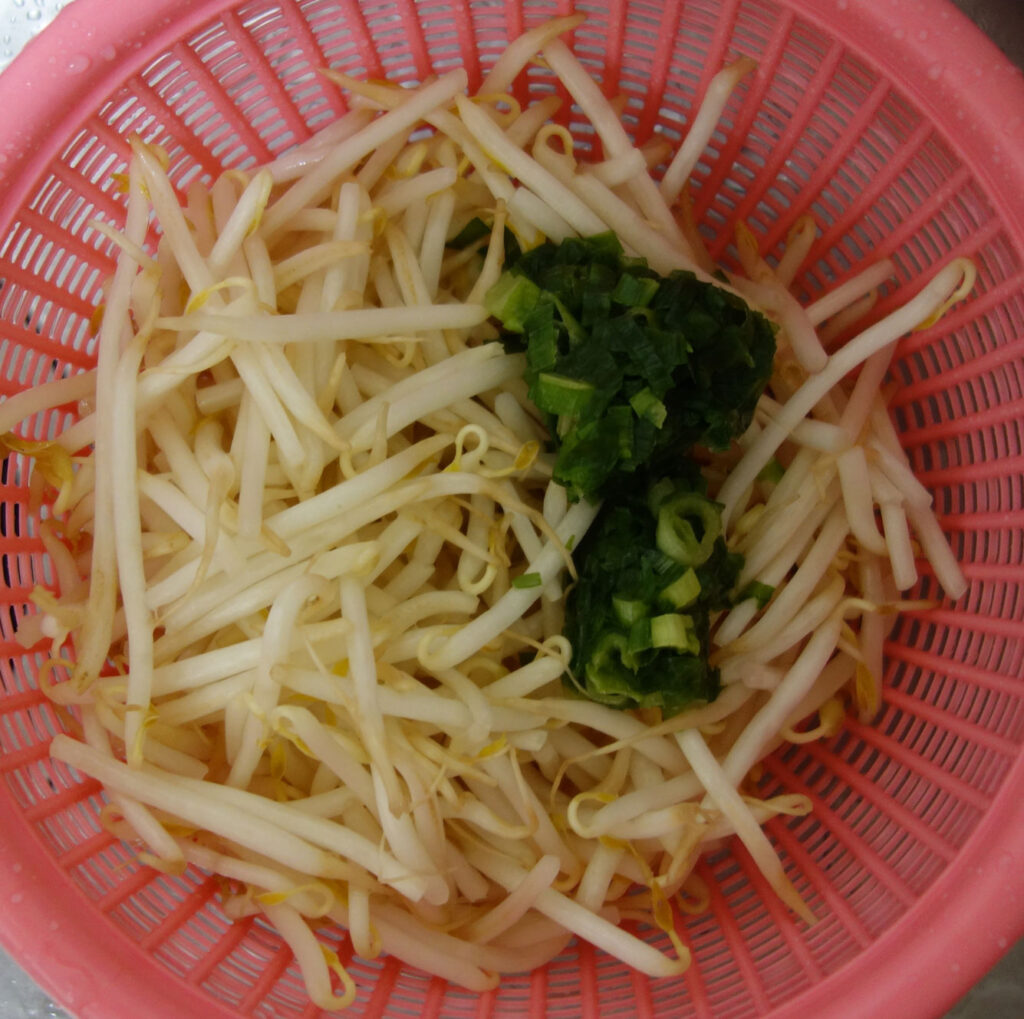 ピンク色のザルに入ったもやしとネギ