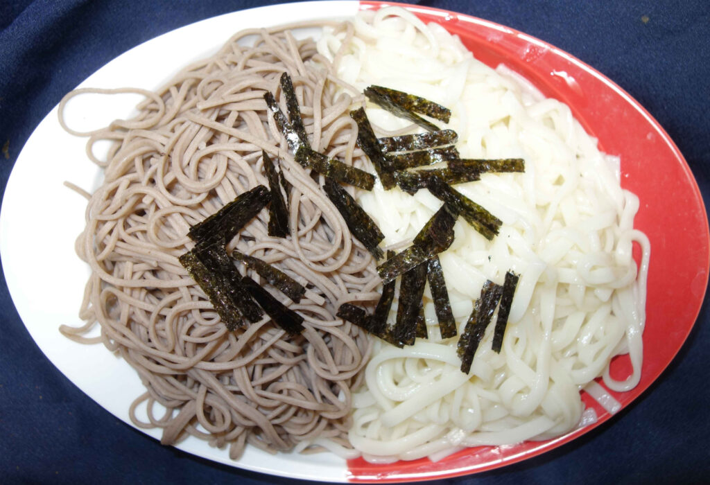 一枚の皿に盛られたそばとうどん海苔が添えられている