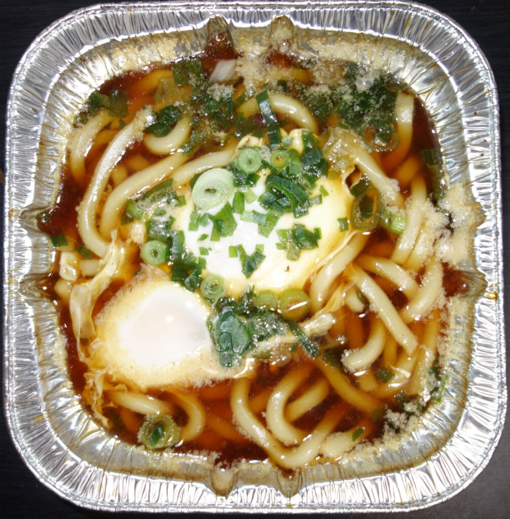 アルミ容器に入った卵とネギが乗ったうどん