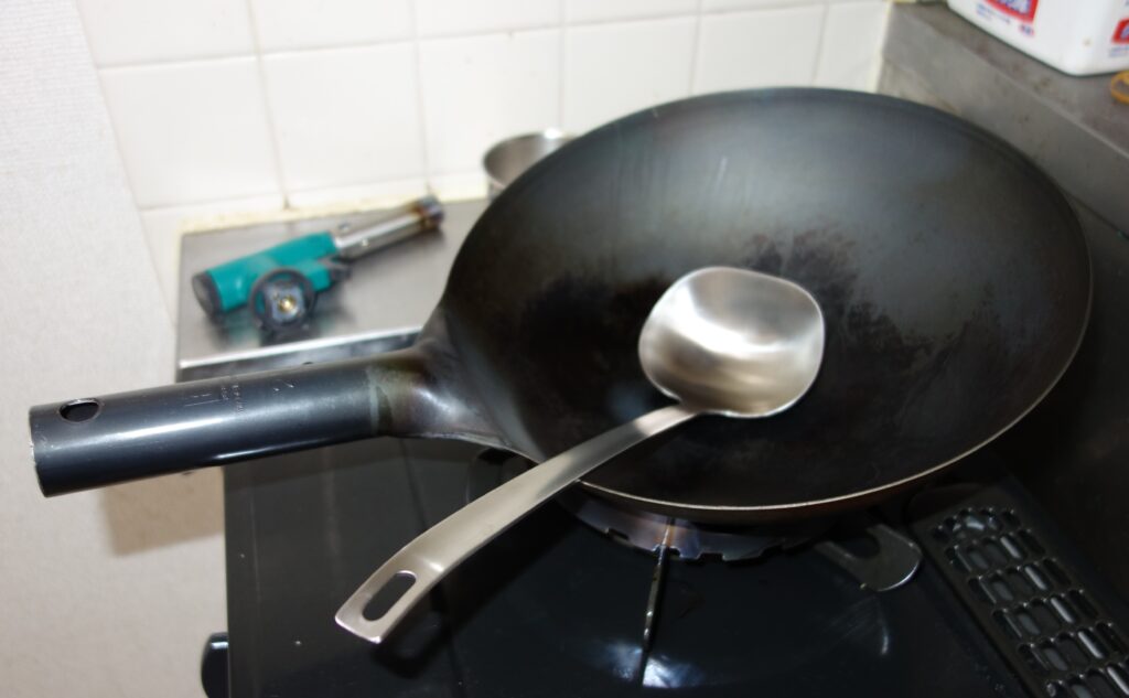 ガスコンロの上の鉄製中華鍋とステンレスのお玉