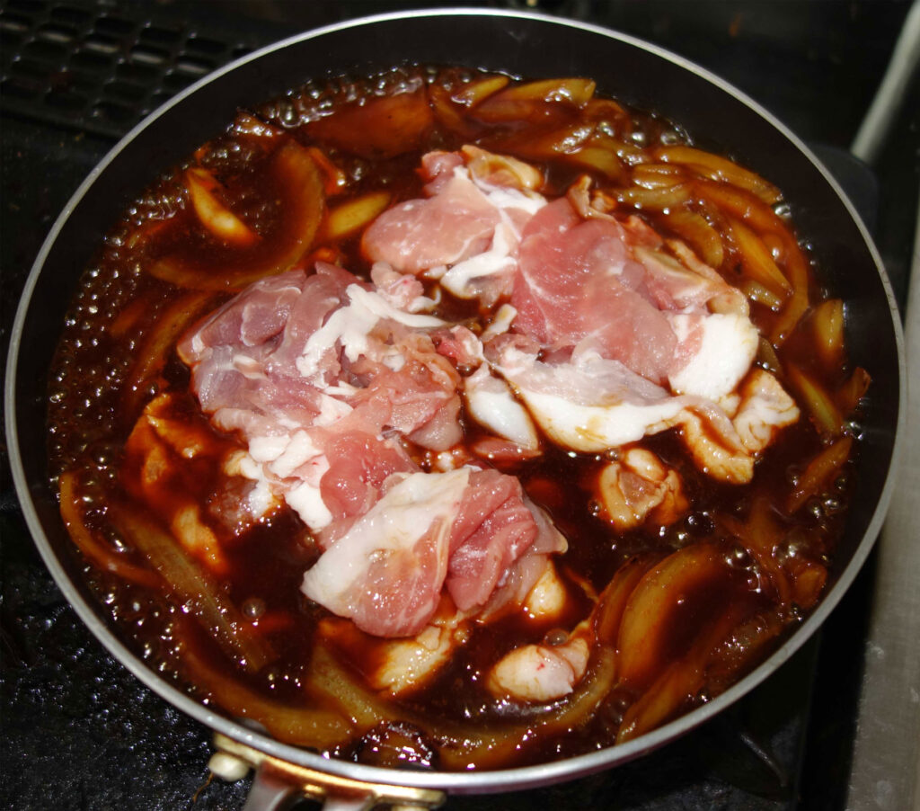 豚肉と玉ねぎを甘辛いタレで煮ている様子