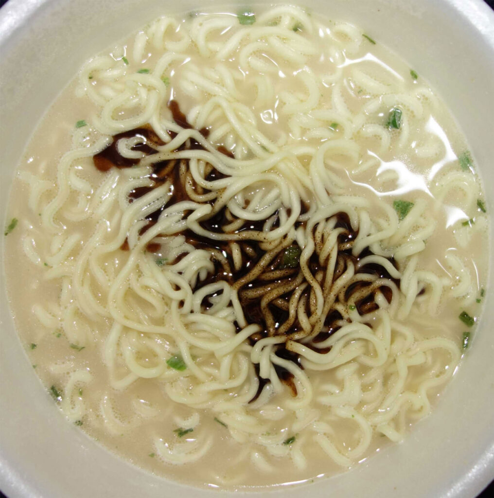 カップに入った白いスープのラーメンに黒いタレがかかっている様子