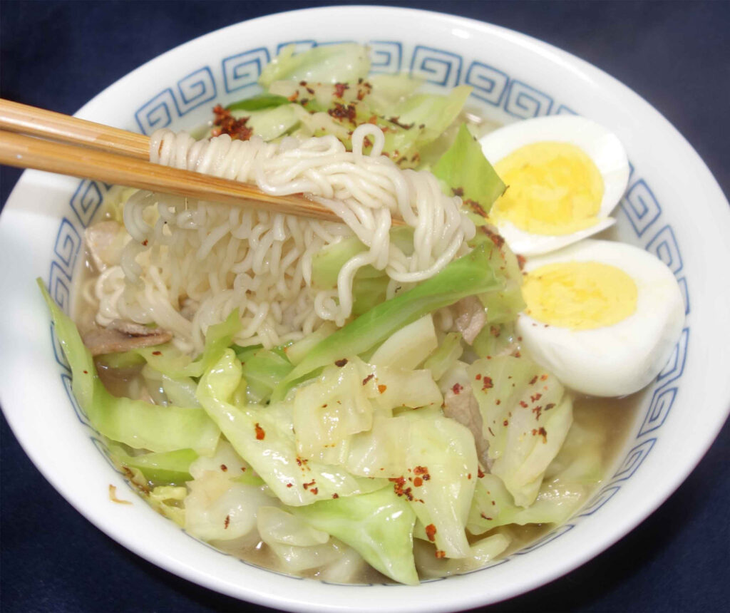 キャベツと煮卵が入ったラーメンを箸で持ち上げている様子