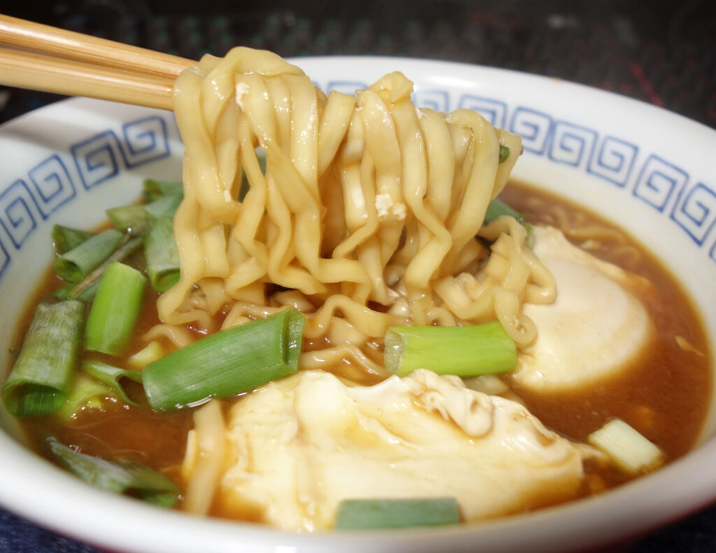 箸で持ち上げられた卵とネギ入りのラーメン